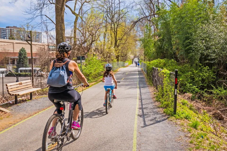 Family wearing helmets rides down separated bike trail in city.
